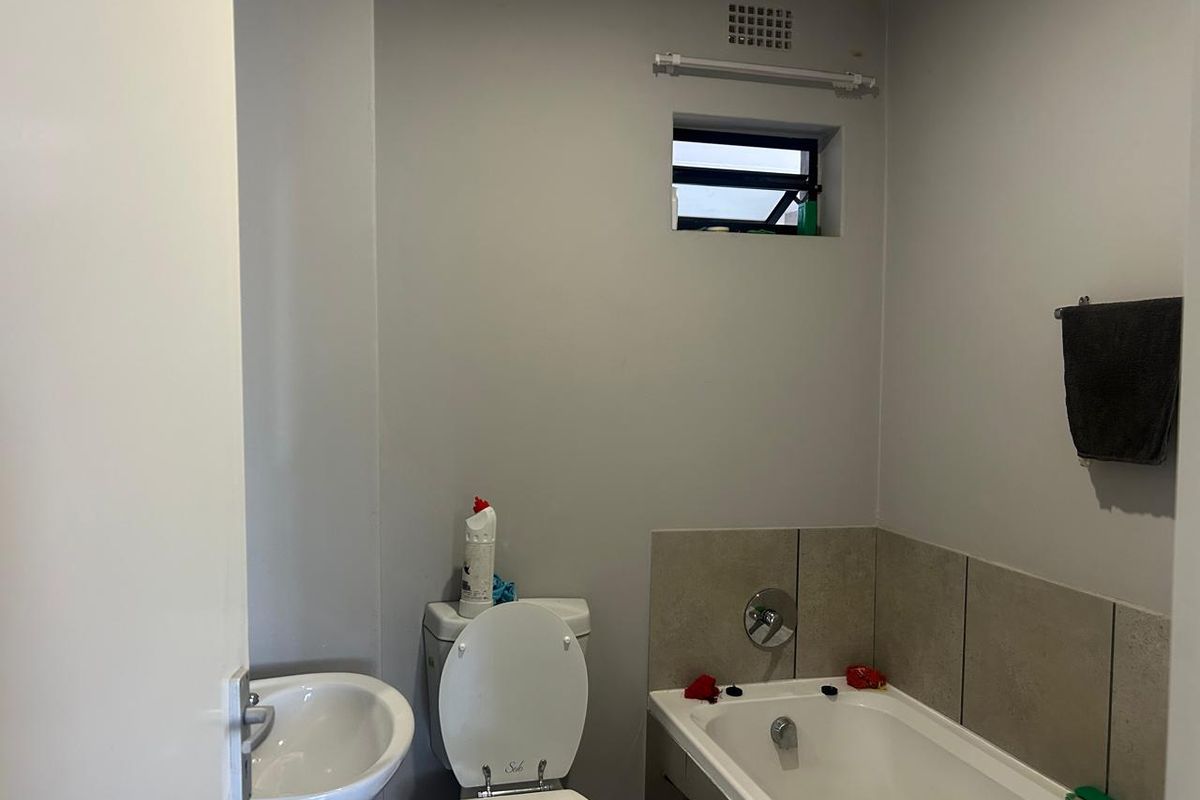 A functional bathroom featuring a standard bathtub, wall-mounted basin, and toilet, with neutral wall finishes and a small ventilation window.