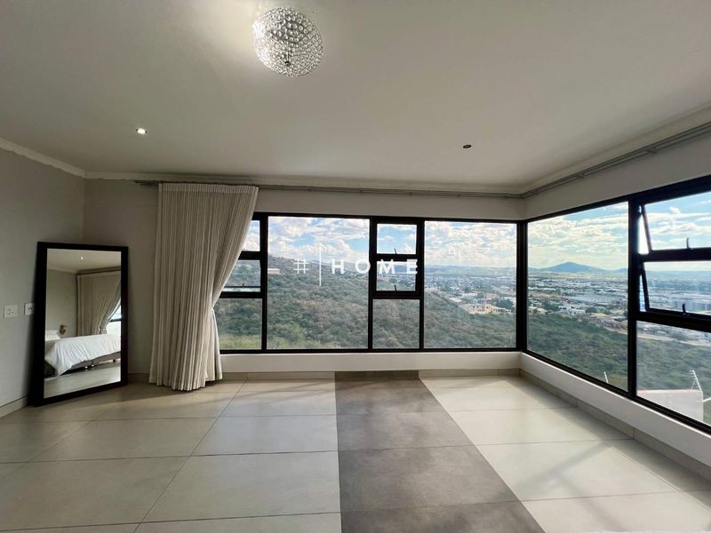 Spacious bedroom featuring large format floor tiles, expansive corner windows with panoramic views, and modern recessed lighting.