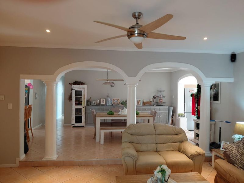Spacious open-plan living and dining area featuring arched architectural details, decorative columns, tiled flooring, and a modern ceiling fan.