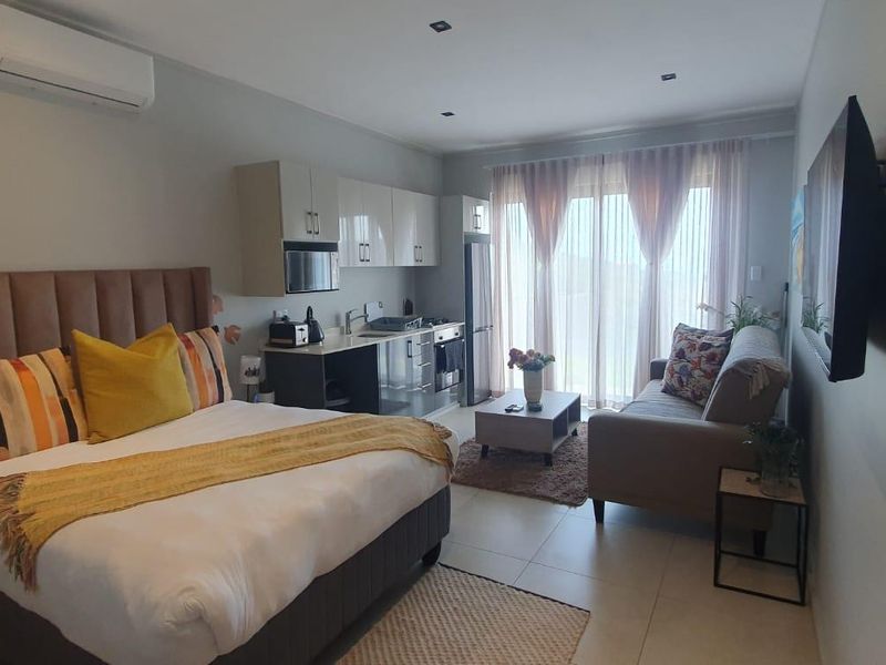 A modern open-plan studio apartment featuring a compact kitchenette, tiled flooring, and direct access to a balcony through sliding glass doors.