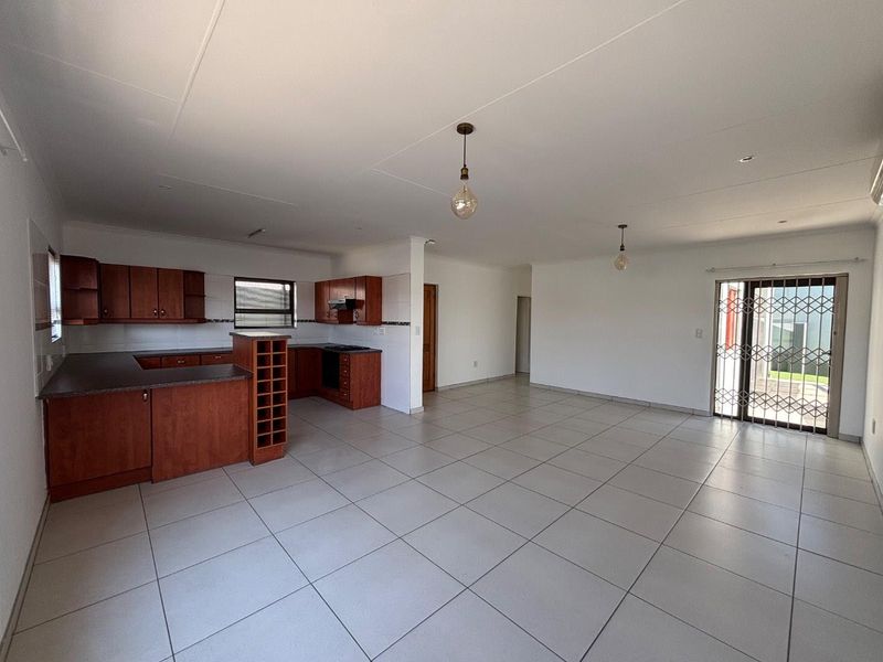Spacious open-plan living area featuring a kitchen with built-in cabinetry, oven, and extractor fan, leading to a tiled living space with security gate access.