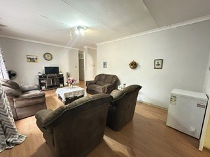 A living room featuring laminate flooring and a ceiling fan, showing signs of wear including visible cracks in the ceiling plaster.