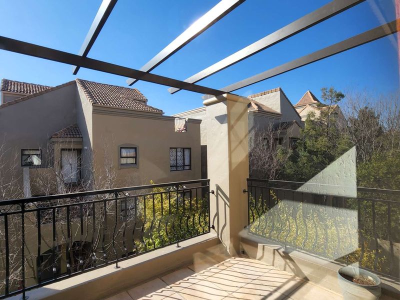A private balcony featuring tiled flooring, a metal pergola structure, and decorative wrought iron railings overlooking the surrounding apartment complex.