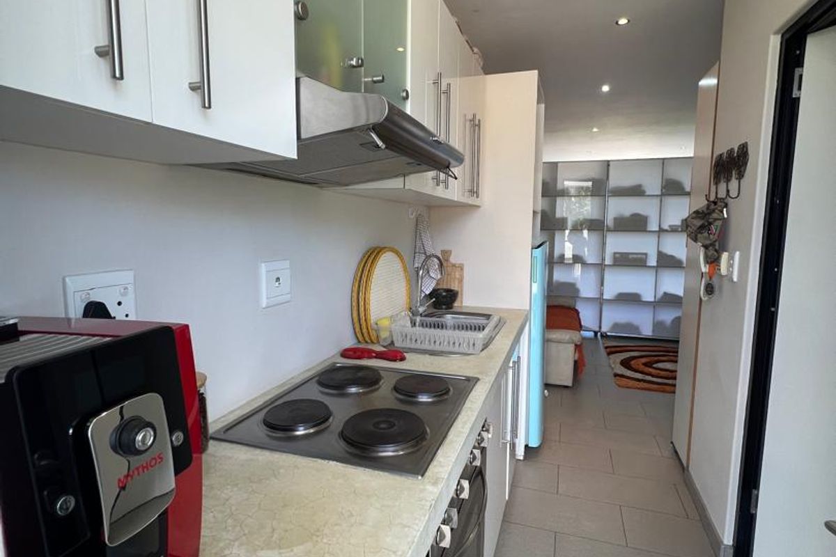 A functional galley-style kitchen featuring built-in cabinetry, a four-plate electric hob, an integrated oven, and an extractor fan, leading into an open-plan living area.