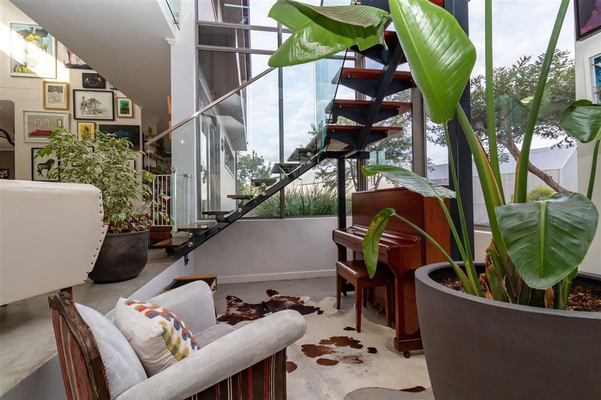 Modern living area featuring a striking floating staircase with glass balustrades, polished concrete flooring, and expansive floor-to-ceiling windows.