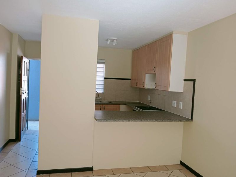 A functional kitchen featuring laminate cabinetry, a built-in hob, tiled backsplash, and a breakfast bar counter, presented in a clean, empty space.