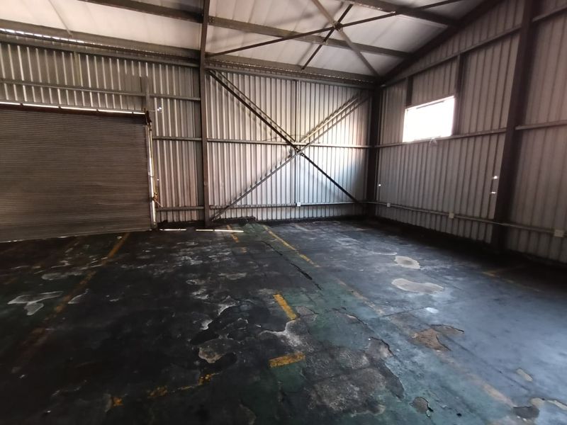 Spacious industrial utility space featuring high-clearance steel portal frame construction, corrugated metal walls, and a large roller shutter door.