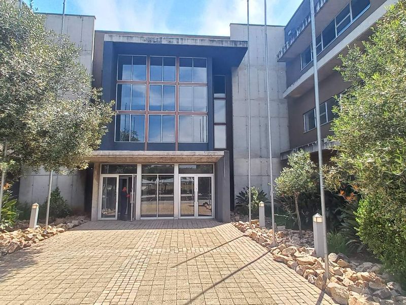 Front entrance view of a modern office building featuring a paved walkway, glass facade, and concrete architectural elements.
