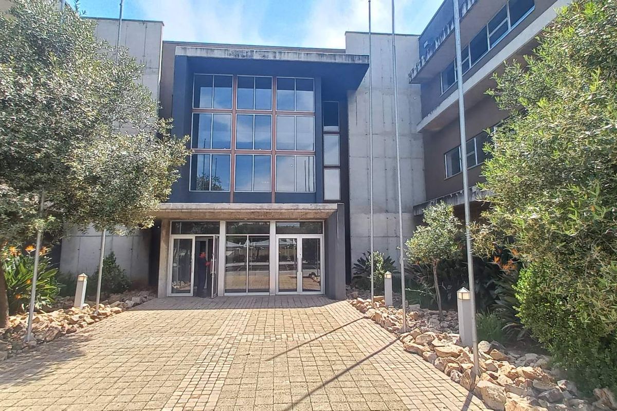 Front entrance view of a modern office building featuring a paved walkway, glass facade, and concrete architectural elements.