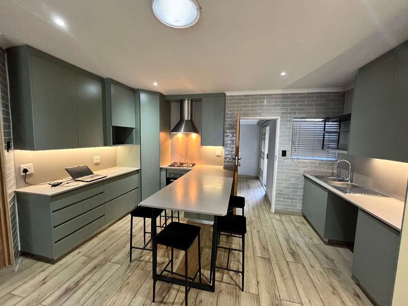 Modern kitchen featuring sage green cabinetry, stone countertops, a central breakfast island, gas hob, and stylish brick-style wall tiling with wood-look flooring.