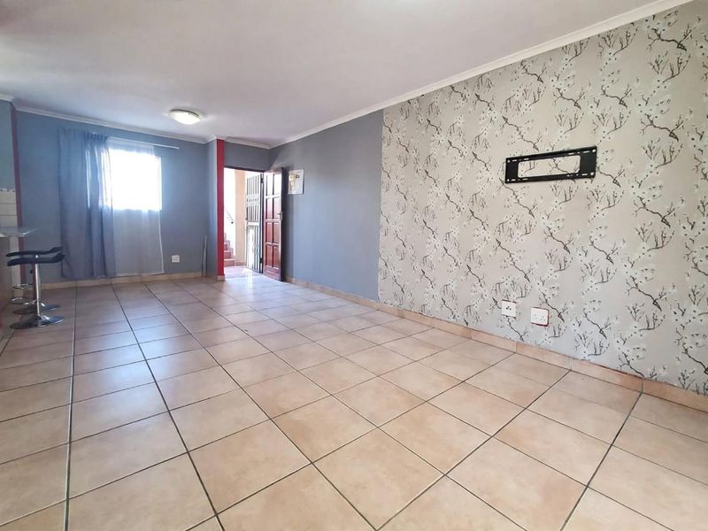 An open-plan living area featuring tiled flooring, a decorative wallpaper feature wall, and a wall-mounted television bracket.