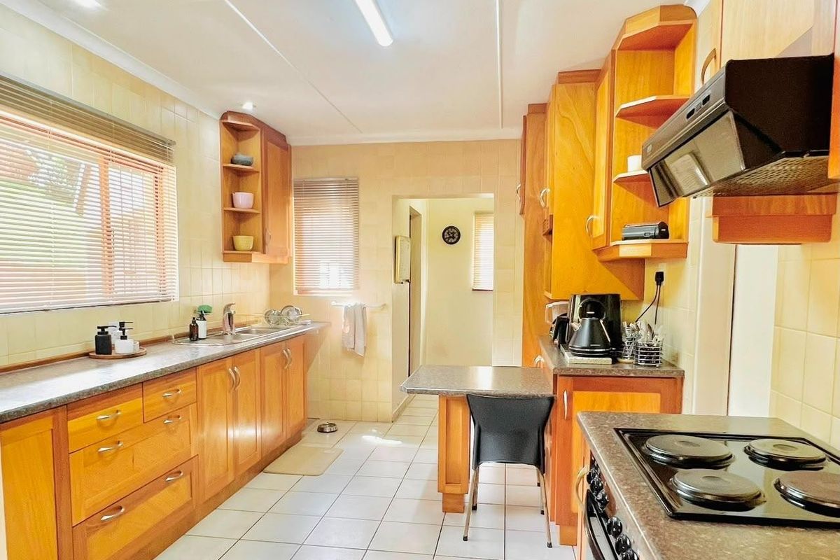 A functional kitchen featuring wooden cabinetry, laminate countertops, tiled splashbacks, and integrated appliances including an electric hob and extractor fan.