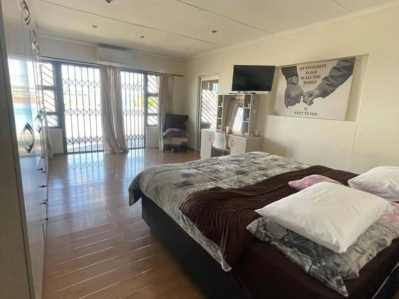 Spacious bedroom featuring built-in cupboards, tiled flooring, recessed lighting, and a split-system air conditioner with direct access to an outdoor area via security gate.