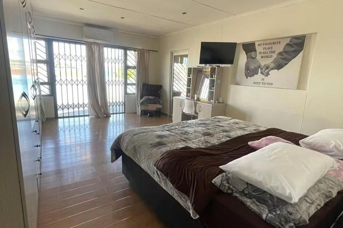Spacious bedroom featuring built-in cupboards, tiled flooring, recessed lighting, and a split-system air conditioner with direct access to an outdoor area via security gate.