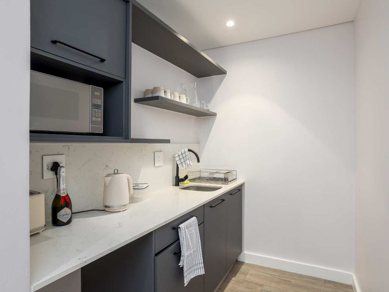 Modern scullery featuring dark grey cabinetry, stone countertops, an undermount sink with a black mixer tap, and integrated microwave.