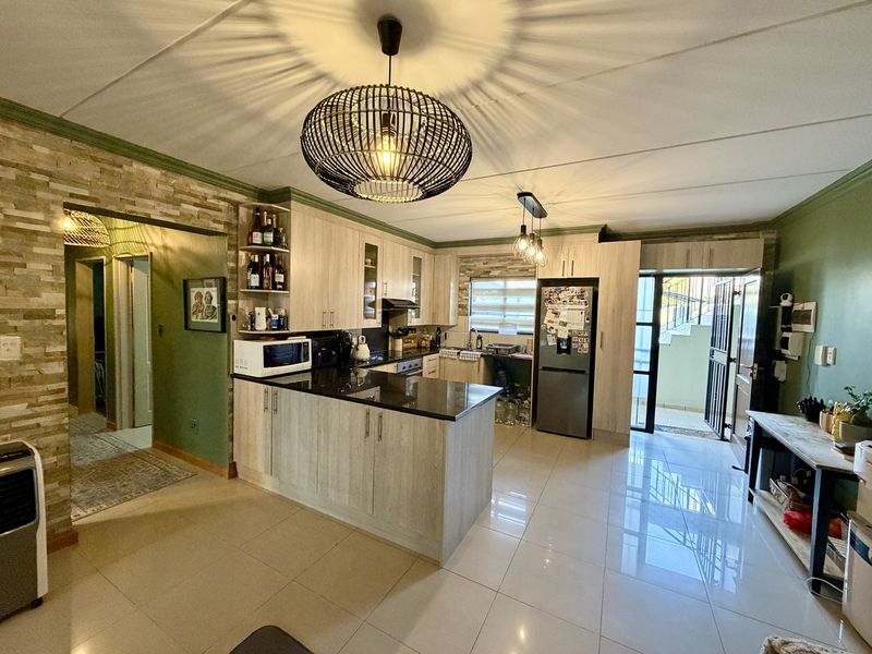 Modern kitchen featuring light wood-finish cabinetry, granite countertops, a stone veneer accent wall, and polished tile flooring with direct access to an outdoor area.