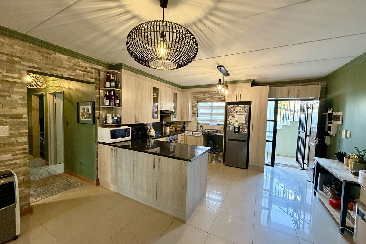Modern kitchen featuring light wood-finish cabinetry, granite countertops, a stone veneer accent wall, and polished tile flooring with direct access to an outdoor area.