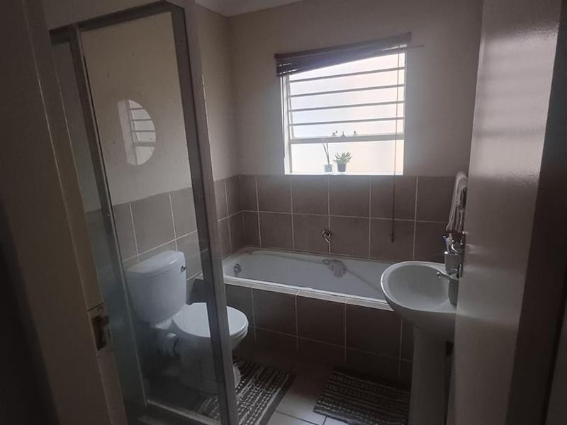 A functional bathroom featuring a shower enclosure, bathtub, pedestal basin, and toilet with neutral tiled finishes and natural light.