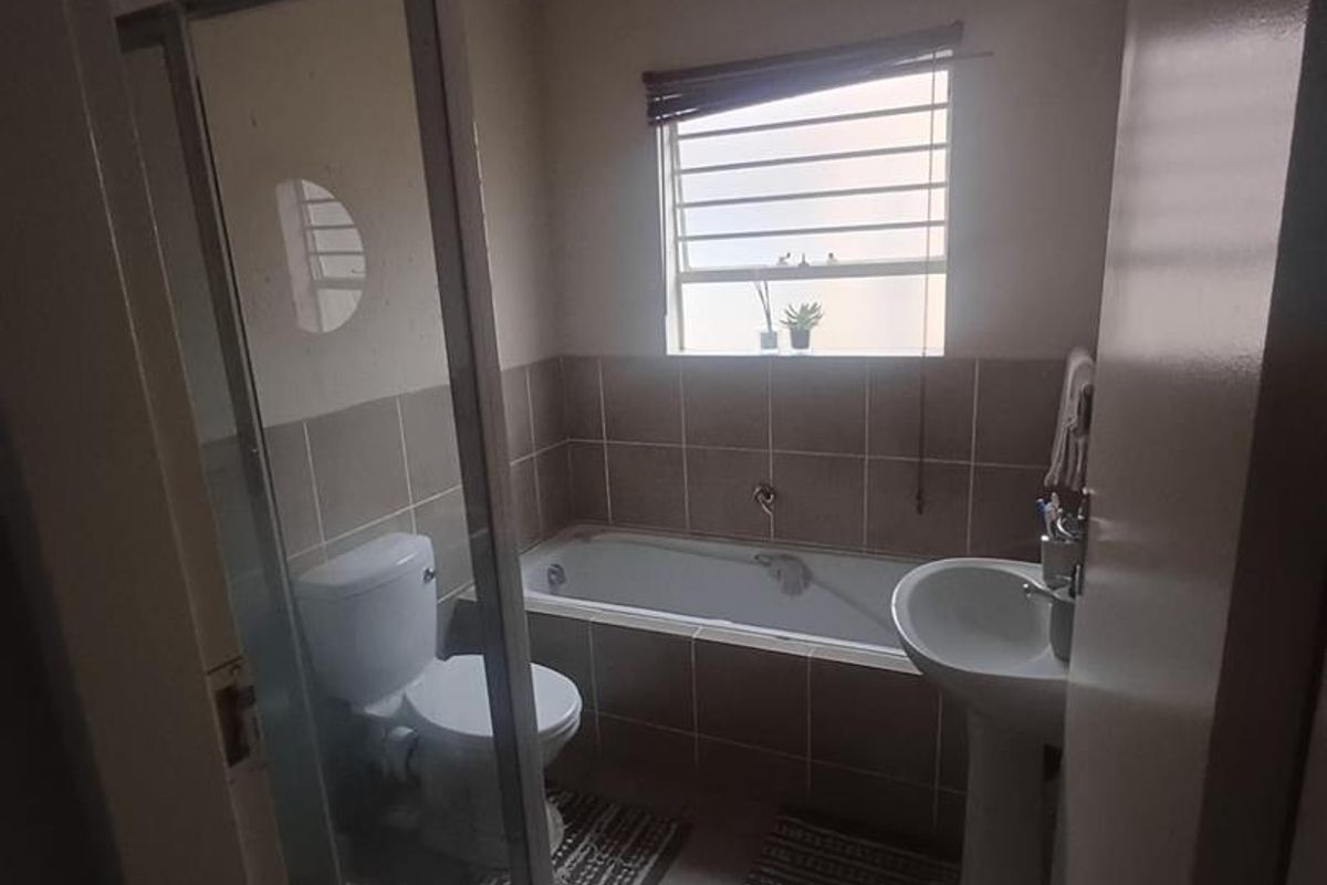 A functional bathroom featuring a shower enclosure, bathtub, pedestal basin, and toilet with neutral tiled finishes and natural light.