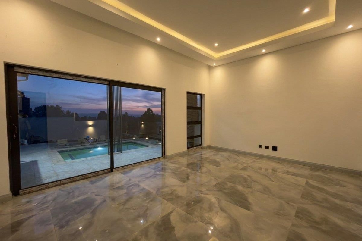 Spacious, modern living area featuring polished marble-look flooring, recessed cove lighting, and large sliding glass doors offering a view of the pool area.