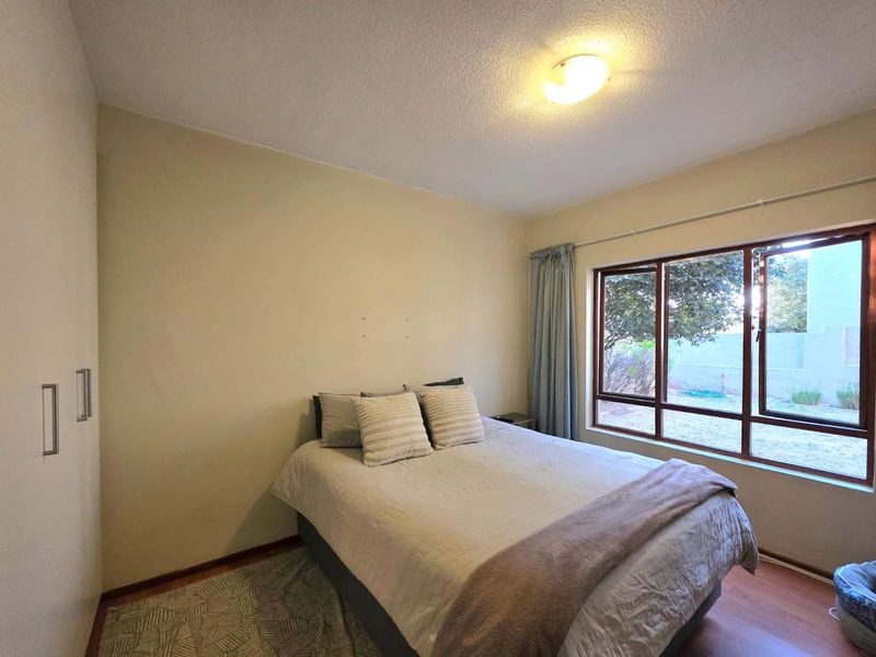 A functional bedroom featuring built-in cupboards, laminate flooring, and a large window providing natural light and garden views.