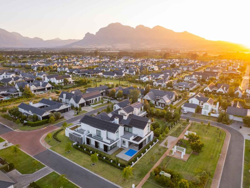Aerial view of a modern residential estate featuring homes with solar panels, private swimming pools, and well-maintained landscaped gardens at sunset.