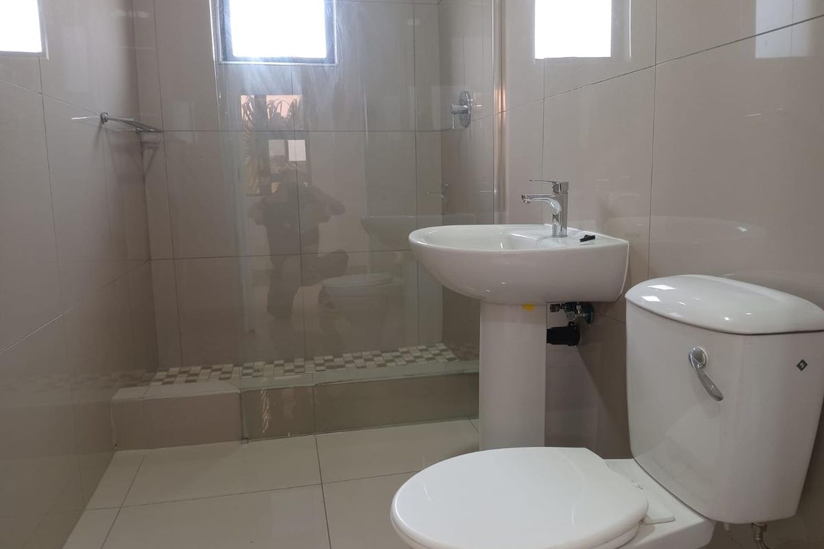 A clean, modern bathroom featuring a pedestal basin, a white toilet, and a glass-enclosed shower with neutral wall and floor tiling.