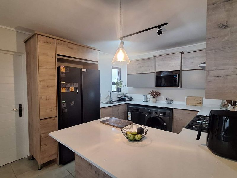 Modern kitchen featuring wood-grain cabinetry, white quartz countertops, integrated appliances, and a functional breakfast bar layout with contemporary lighting.