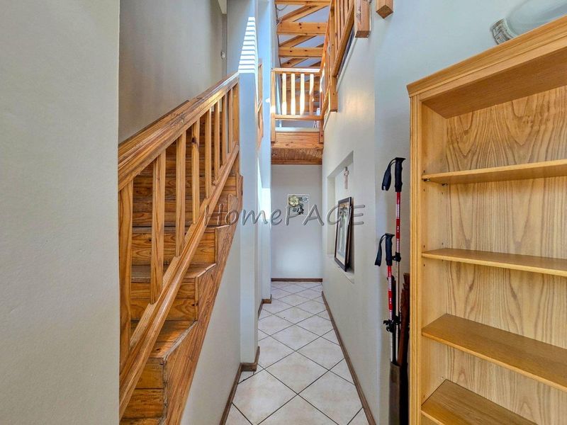 A narrow hallway featuring a wooden staircase with a matching balustrade and tiled flooring, leading to an upper level landing.