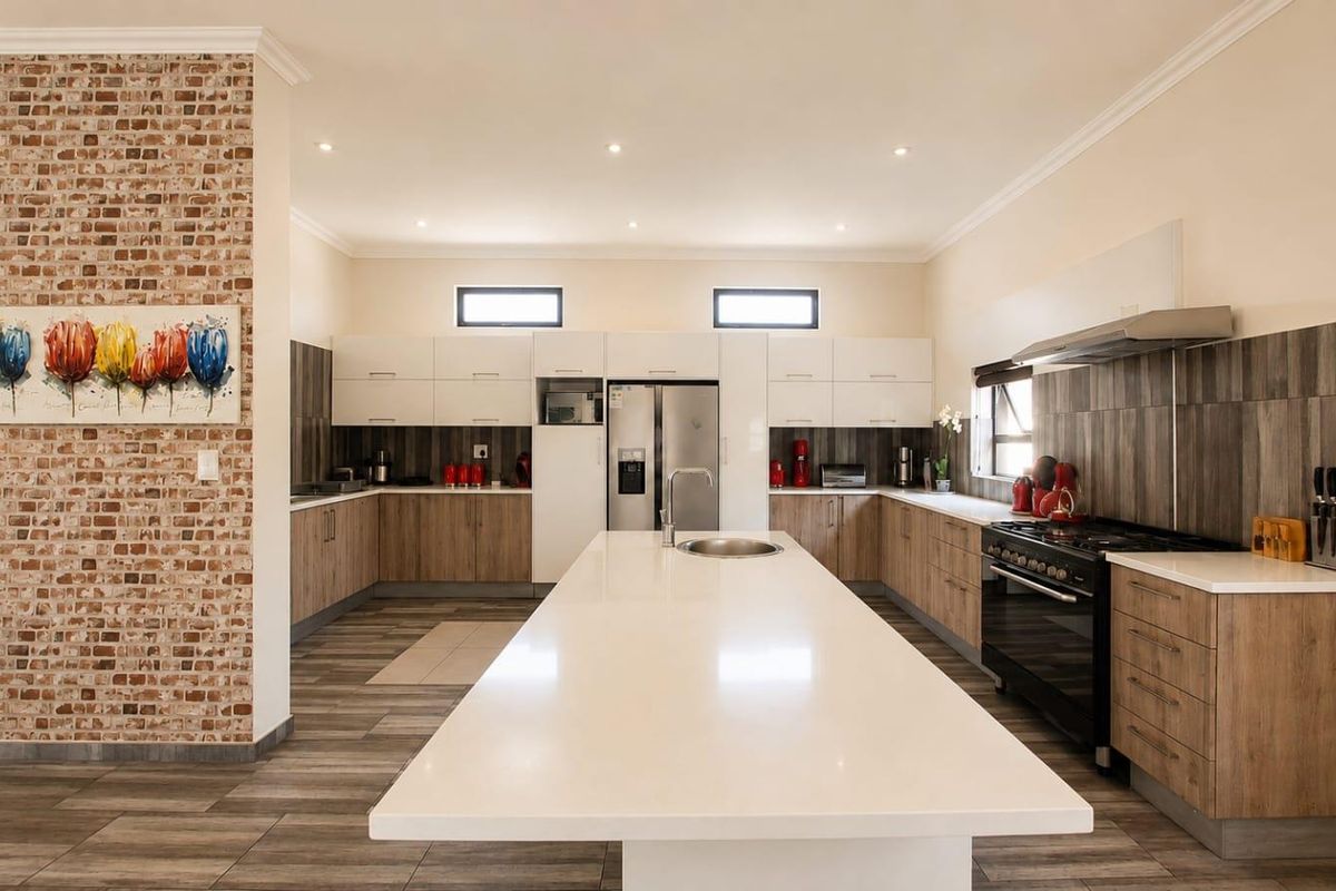 Modern kitchen featuring a large central island with quartz countertops, built-in oven, gas cooktop, and a stylish exposed brick feature wall.