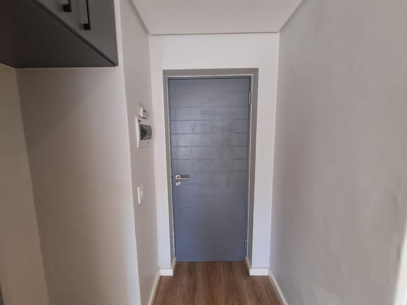 A clean, well-maintained hallway featuring laminate flooring, a modern grey internal door, and a wall-mounted intercom system.