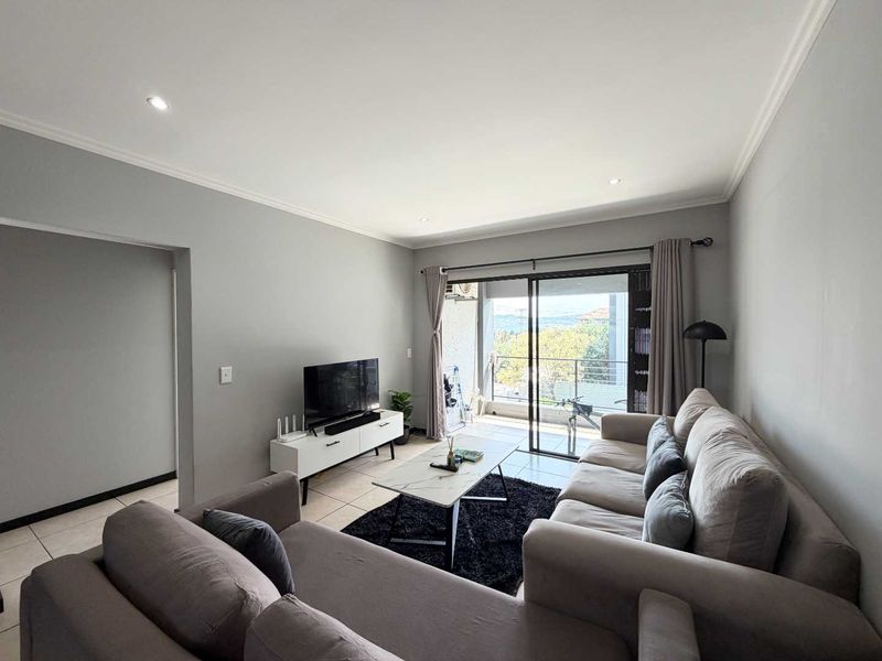 A well-maintained living room featuring neutral walls, tiled flooring, recessed lighting, and direct access to a balcony through sliding glass doors.