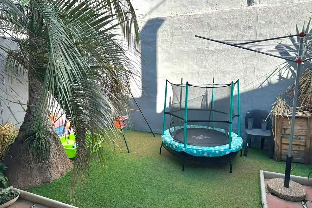 A compact rear courtyard area featuring artificial turf, a boundary wall, and paved edging, suitable for outdoor play or relaxation.
