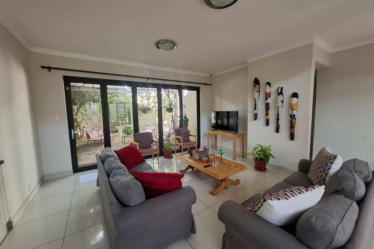 Spacious living room featuring large black-framed sliding glass doors that open onto a private rear patio area, finished with neutral floor tiles.