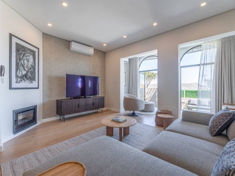 Modern living room featuring hardwood flooring, a built-in fireplace, split-system air conditioning, and large arched windows providing natural light and access to the patio.