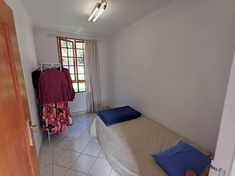 A compact bedroom featuring tiled flooring, a timber-framed window, and a simple ceiling light fixture, offering a functional space for a single bed.
