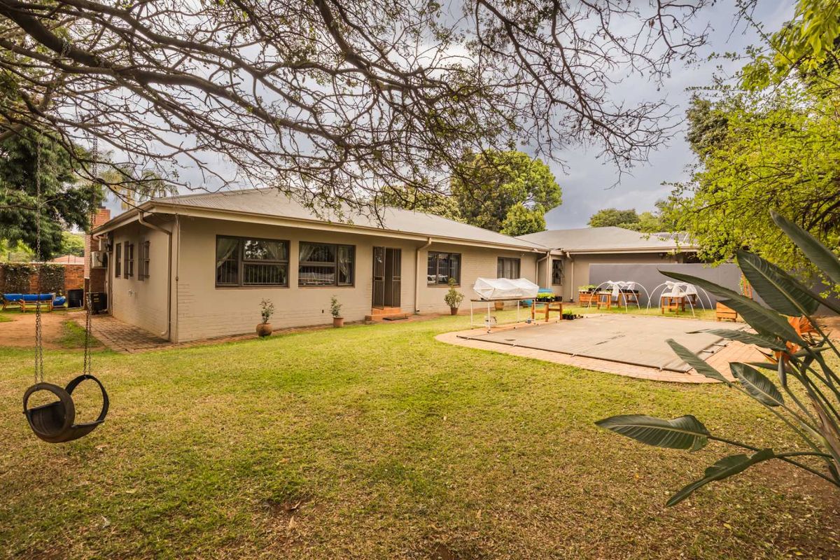 Rear view of the house featuring a spacious lawn, a covered swimming pool, and a paved patio area.