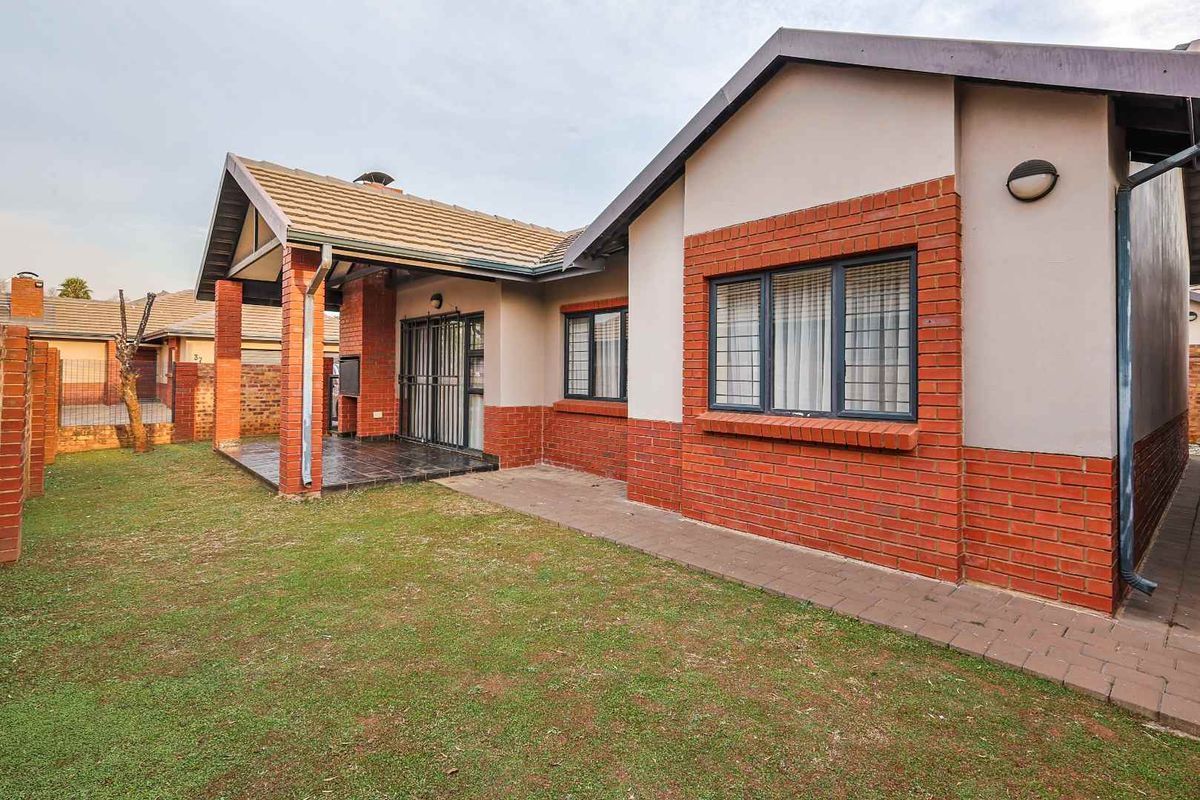 Rear view of the townhouse featuring a covered patio with a built-in braai, brick facade, and a private garden area.