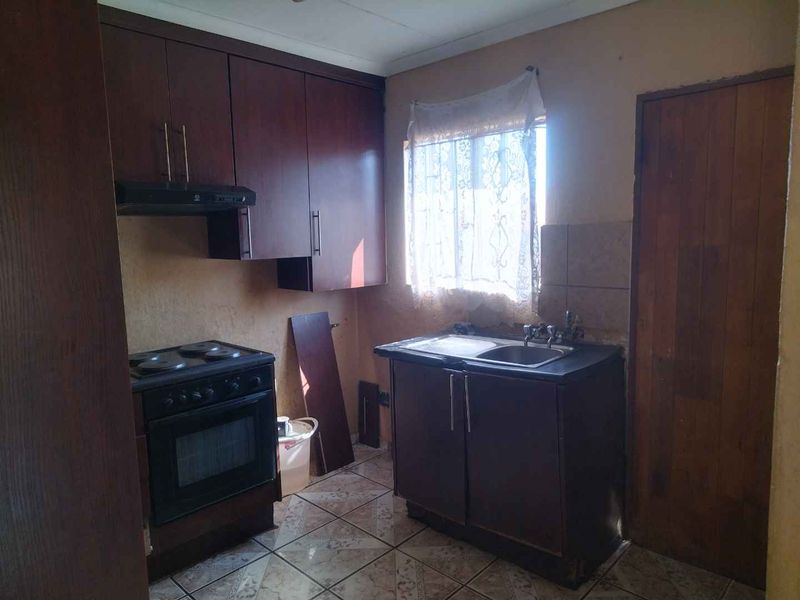 A compact kitchen featuring dark wood cabinetry, an electric stove with extractor fan, and a double sink with tiled splashback.