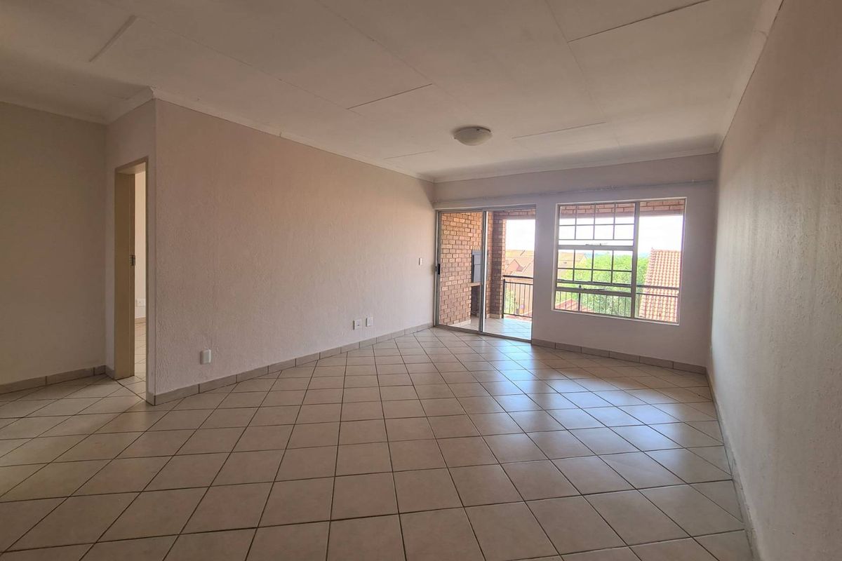 Spacious, empty living area featuring neutral tiled flooring, large windows, and a sliding door leading to an outdoor balcony.