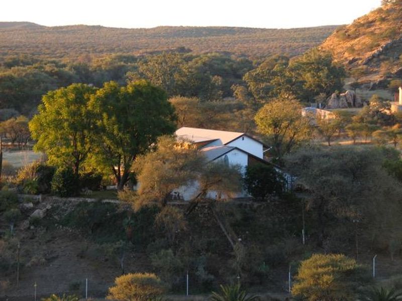 An elevated aerial view of a residential property nestled within a natural, hilly landscape featuring mature trees and scenic surroundings.