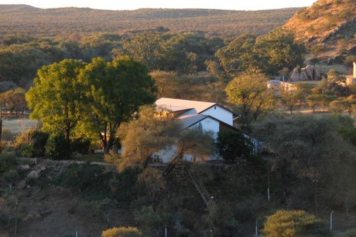 An elevated aerial view of a residential property nestled within a natural, hilly landscape featuring mature trees and scenic surroundings.
