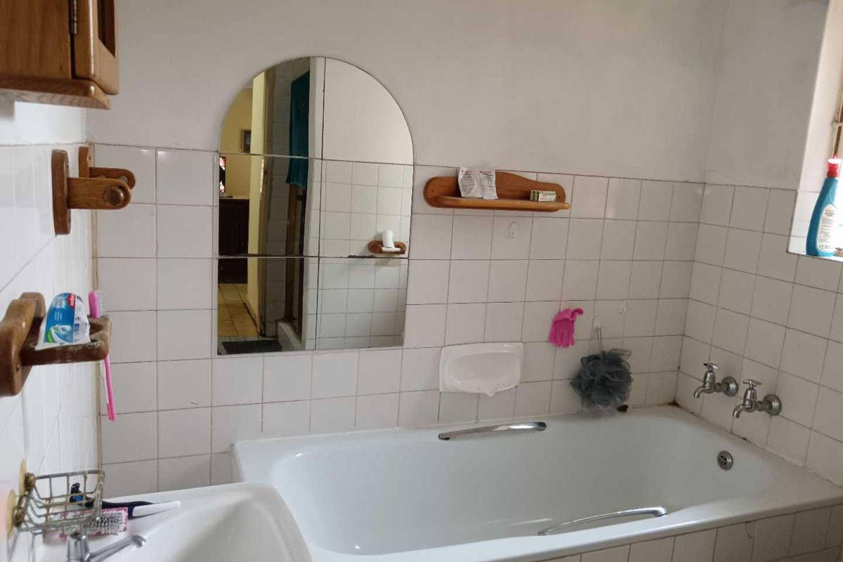 A dated bathroom featuring a standard bathtub, wall-mounted basin, and tiled walls, offering potential for a modern renovation.