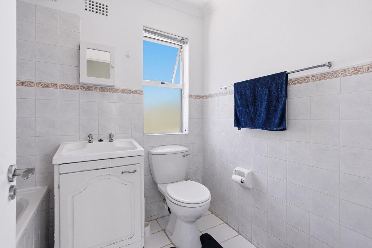 A functional bathroom featuring a vanity cabinet, toilet, and tiled walls with a neutral finish, offering potential for modern updates.