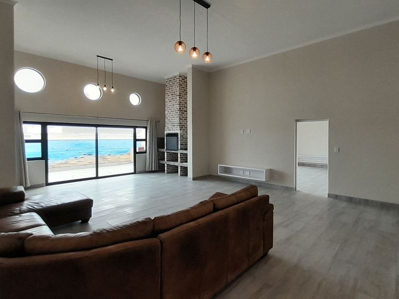 Spacious living room featuring high ceilings, a brick fireplace, large sliding doors with ocean views, and modern tile flooring.