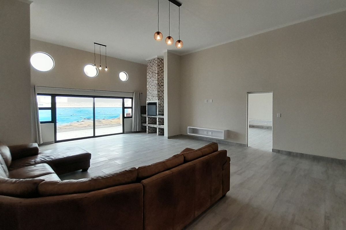 Spacious living room featuring high ceilings, a brick fireplace, large sliding doors with ocean views, and modern tile flooring.