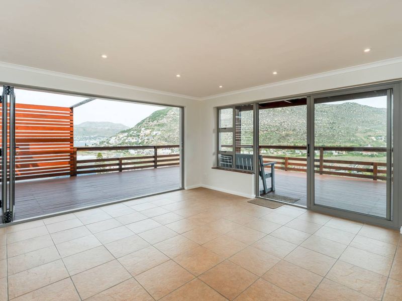 Spacious living area featuring large aluminium stacker and sliding doors opening onto a timber deck with expansive mountain and coastal views.