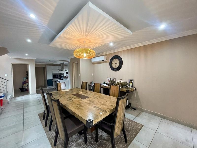 Open-plan dining area featuring tiled flooring, a recessed ceiling with feature lighting, and an integrated kitchen visible in the background.