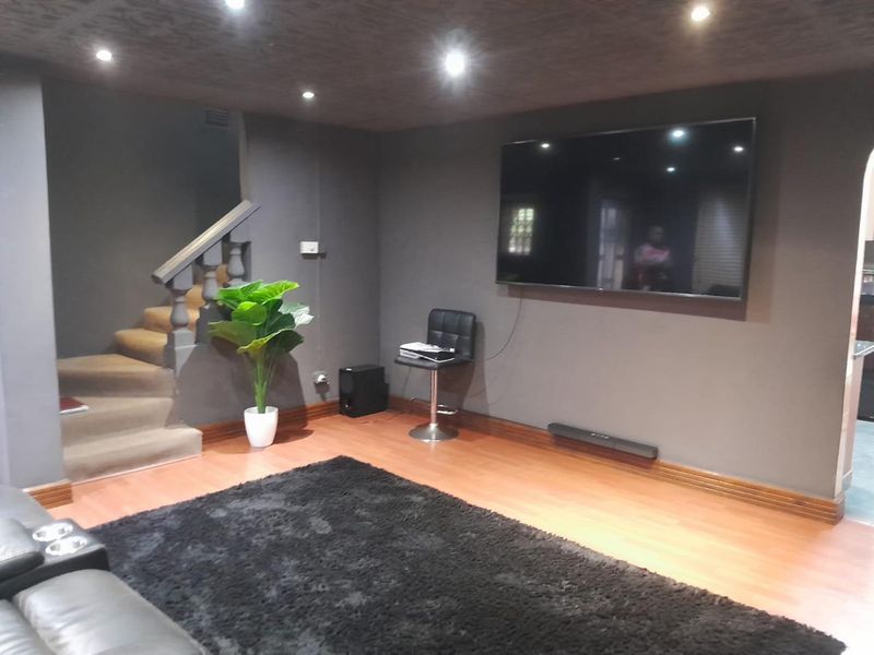 A living room featuring laminate flooring, recessed downlighting, and an integrated staircase with a balustrade.