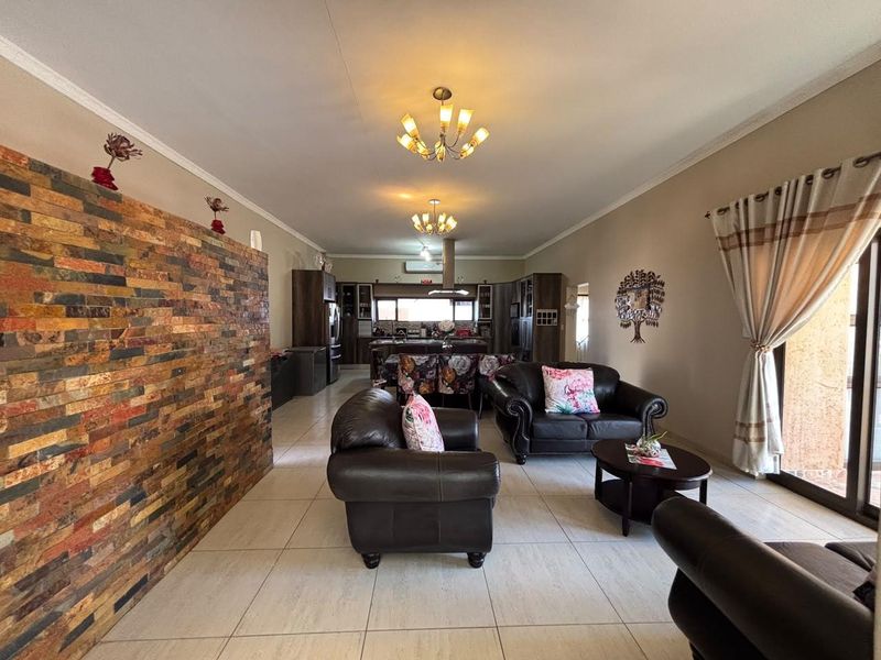 Spacious open-plan living and kitchen area featuring a decorative stone feature wall, neutral tiled flooring, and modern kitchen cabinetry with an island.